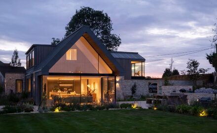large glass gable end window shown at night with frameless triangular window and sliding doors