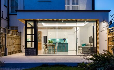 banner image of an extension in London using sliding glass doors with steel windows shown at night